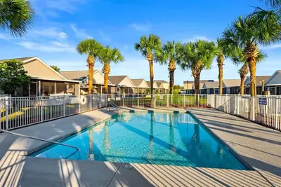 a swimming pool with palm trees and a fence at Charming house near the beach in Panama City Beach