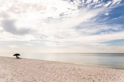 a person sitting under an umbrella on a beach at Glory Days 30A - Pool, Bikes & Close Beach Access in Inlet Beach