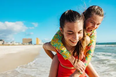 two girls are sitting on the beach at The Barefoot Hotel in Panama City Beach