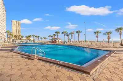 a swimming pool next to a beach with palm trees at The Summit 922 - Relaxation meets the Shoreline in Panama City Beach