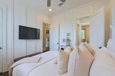 a white bed with pillows and a tv on a wall at Driftwood - Vacation Home Near the Beach with a Large Outdoor Area in Santa Rosa Beach