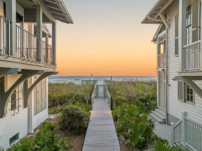a boardwalk between two buildings with the ocean in the background at YOLO Carriage in Rosemary Beach
