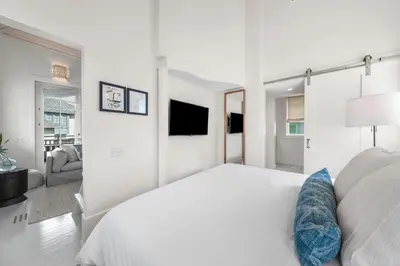 a white bedroom with a bed and a tv at YOLO Carriage in Rosemary Beach