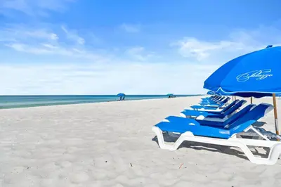 a row of blue chairs and an umbrella on a beach at Palazzo Beach Resort by Panhandle Getaways in Panama City Beach