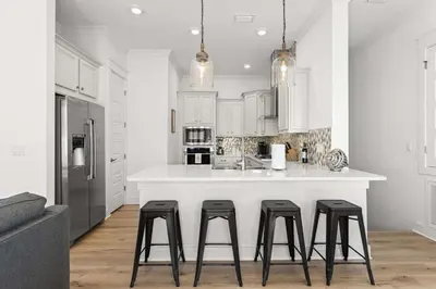 a kitchen with white cabinets and a counter with stools at Rhema Luxury Beach Haus 2BR 2B ResortPool with optional 6-seater GolfCart & 4Bikes in Inlet Beach