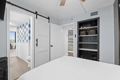 a white bedroom with a bed and a bathroom at PCB Beach Gateaway On The Sand in Panama City Beach