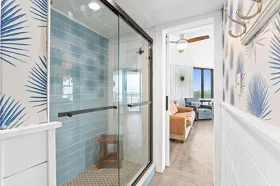 a glass shower in a bathroom with a blue tile wall at PCB Beach Gateaway On The Sand in Panama City Beach