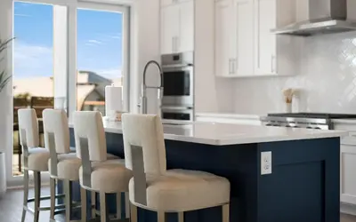 a kitchen with white cabinets and a blue island with chairs at Magnolia Way in Santa Rosa Beach