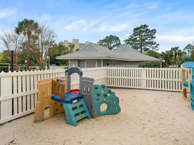 a playground with play equipment in front of a fence at Skinny Dip- Renovated Unit- Steps to the beach in Santa Rosa Beach
