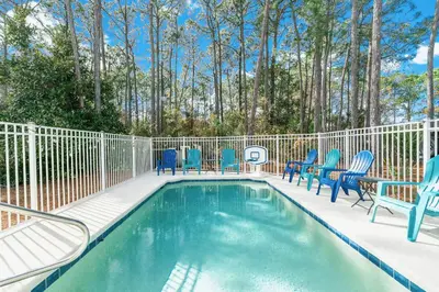 a swimming pool with blue chairs and a fence at Somerset by the Sea by Travel Life Vacations in Santa Rosa Beach