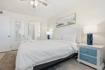 a white bedroom with a large bed and a blue nightstand at The Summit 926 - One Bedroom Beachfront Condo in Panama City Beach