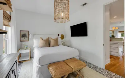a white bedroom with a bed and a tv at Cottage Breeze in Rosemary Beach