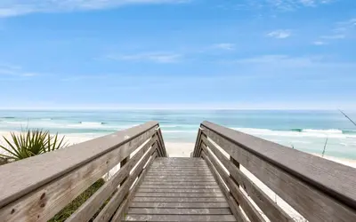 a boardwalk to the beach with the ocean in the background at Cottage Breeze in Rosemary Beach