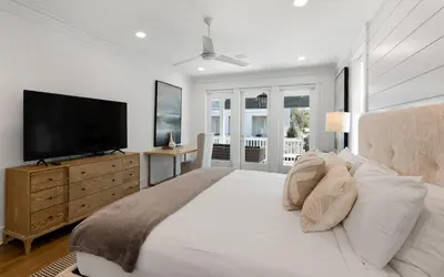 a white bedroom with a large bed with a flat screen tv at Out of Office in Santa Rosa Beach