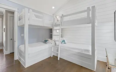 two bunk beds in a white room with wood floors at Pirates Smile in Rosemary Beach