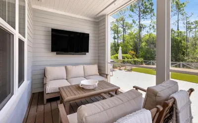 a screened in porch with a tv and a couch and chairs at Surf Sanctuary in Santa Rosa Beach