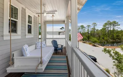 a porch with a swing and an american flag at Surf Sanctuary in Santa Rosa Beach