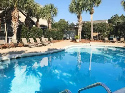 a large blue swimming pool with chairs and palm trees at Rise and Shine in Santa Rosa Beach