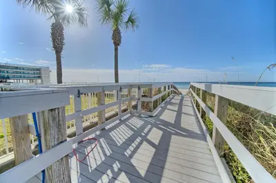 a wooden boardwalk leading to the beach with palm trees at Ocean Reef in Panama City Beach