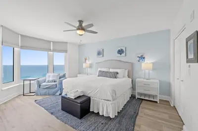 a white bedroom with a bed and a chair at Emerald Beach 1736 by Emerald Coast Retreats in Panama City Beach