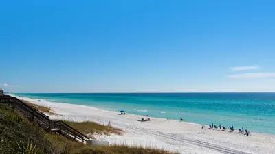 a beach with people sitting on the sand and the ocean at Camelot in Seagrove Beach