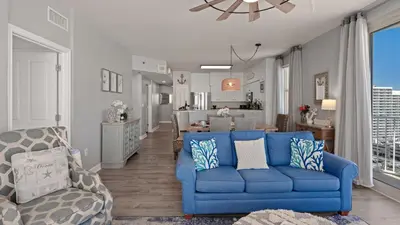 a living room with a blue couch and a kitchen at Emerald Horizon by AvantStay Beachfront Condo Resort Pool Gulf Balcony Views Near Pier Park Dining in Panama City Beach