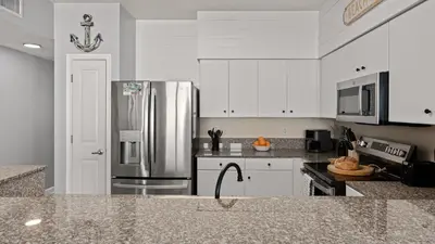a kitchen with white cabinets and a stainless steel refrigerator at Emerald Horizon by AvantStay Beachfront Condo Resort Pool Gulf Balcony Views Near Pier Park Dining in Panama City Beach