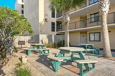 a patio with picnic tables and palm trees in front of a building at Moondrifter 205 in Panama City Beach