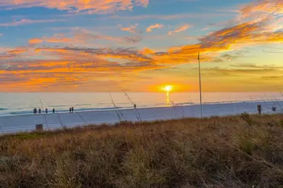 a sunset at the beach with people walking on the beach at Pet Friendly Beach House - Sunset by the Sea in Panama City Beach