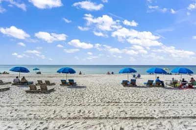 a group of people sitting on a beach with blue umbrellas at The Summit - Family Friendly Vacation! in Panama City Beach
