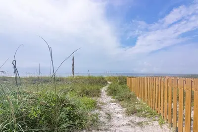 a wooden fence next to a dirt road near the beach at Emerald Seascape! Gulf front! Dog friendly! in Panama City Beach