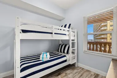 a bunk bed room with white bunk beds and a window at It’s Sea-esta Time! Sleep, Sun, & Sea on the 9th Floor! Sleeps 6! Beachfront! in Panama City Beach