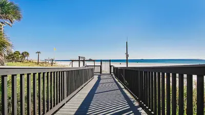 a boardwalk to the beach with a fence and palm trees at Beachfront! Balcony Views! Pools and Beach Access in Panama City Beach