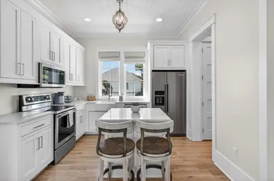 a kitchen with white cabinets and a table with stools at BAH Casa in Inlet Beach