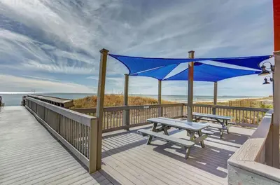 a wooden deck with a picnic table and a blue canopy at Sunrise Beach 17th Floor 3BR Condo | Oversized Balcony, Heated Pool, Near Pier Park in Panama City Beach