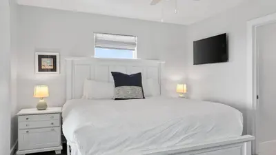a white bedroom with a white bed and a tv at Sandy Pelican by AvantStay Exclusive Beach Access Private Pool Firepit Balcony Sunset Views in Seacrest