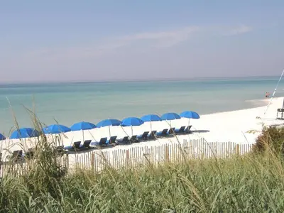a line of chairs with blue umbrellas on a beach at Seychelles 701 by Emerald Coast Retreats in Panama City Beach