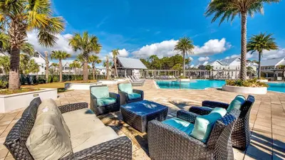 a patio with chairs and a pool with palm trees at Prominence 14B in Rosemary Beach