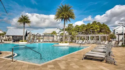 a swimming pool with lounge chairs and palm trees at Prominence 14B in Rosemary Beach