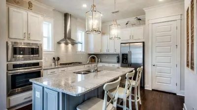 a kitchen with white cabinets and a large island with chairs at Prominence 14B in Rosemary Beach