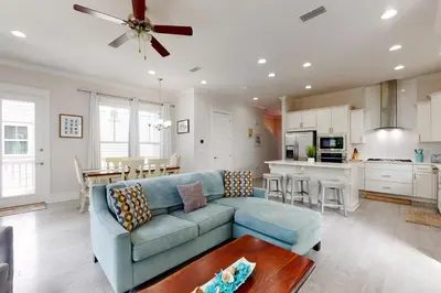 a living room with a blue couch and a kitchen at Lovely Two-Story Home with Porches Access to Pool & Dock in Inlet Beach