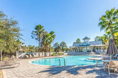 a swimming pool with tables and chairs and a building at Lovely Two-Story Home with Porches Access to Pool & Dock in Inlet Beach