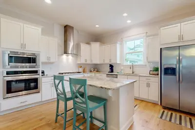 a kitchen with white cabinets and a island with two green chairs at Brand-new house on Powell Lake near beach & 30A with pool W&D & gym in Inlet Beach
