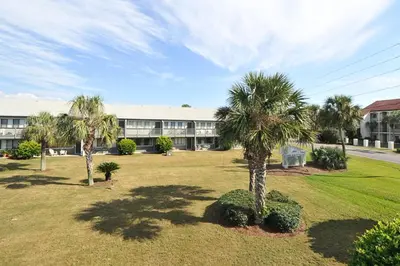 a building with palm trees in front of a yard at Beautiful coastal studio condo with pool in Santa Rosa Beach