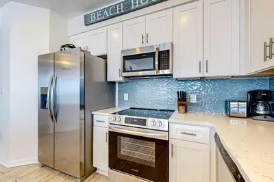 a kitchen with white cabinets and a stainless steel refrigerator at Gulf-front 3-bedroom condo with balconies off each bedroom & pickleball in Santa Rosa Beach
