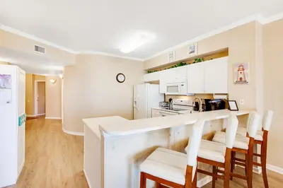 a kitchen with white cabinets and a bar with stools at Charming suite with spacious balcony pools tennis & pickleball in Santa Rosa Beach