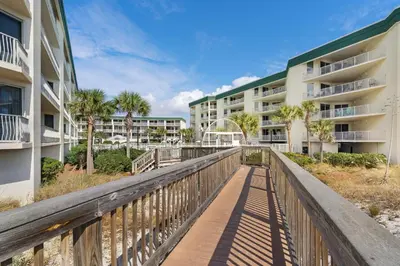 a boardwalk between two apartment buildings with palm trees at Gorgeous 3-bedroom condo with stunning view spacious balcony & pickleball in Santa Rosa Beach