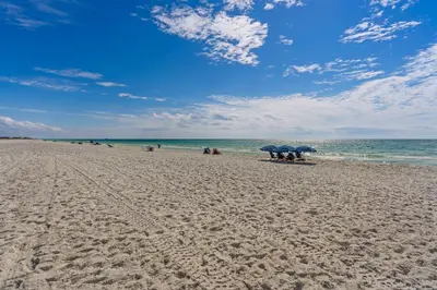 a beach with people sitting under umbrellas and the ocean at Bright Gulf-view condo with balcony pool seasonal beach service & pickleball in Santa Rosa Beach