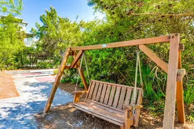a wooden swing sitting in a yard with trees at Amazing Santa Rosa Beach condo with pool hot tub & pickleball in Seacrest