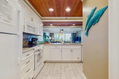 a kitchen with white cabinets and a wooden ceiling at Lovely condo with pool hot tub modern furnishings pickleball - near beach in Seacrest